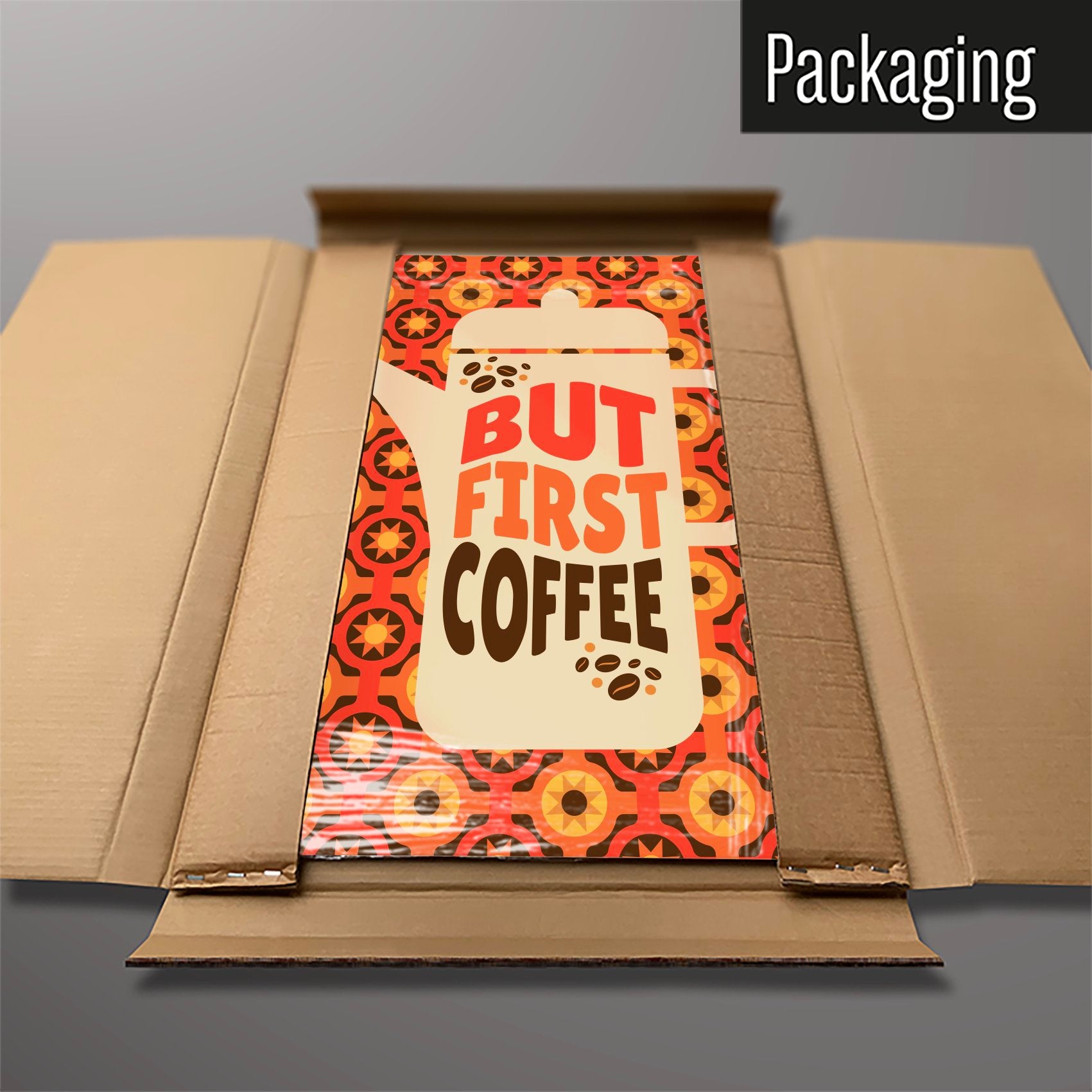 A large magnetic notice board showing a design of a  coffee pot with a quote that reads 'but first coffee' with a seventies style orange and brown pattern behind in cardboard packaging 