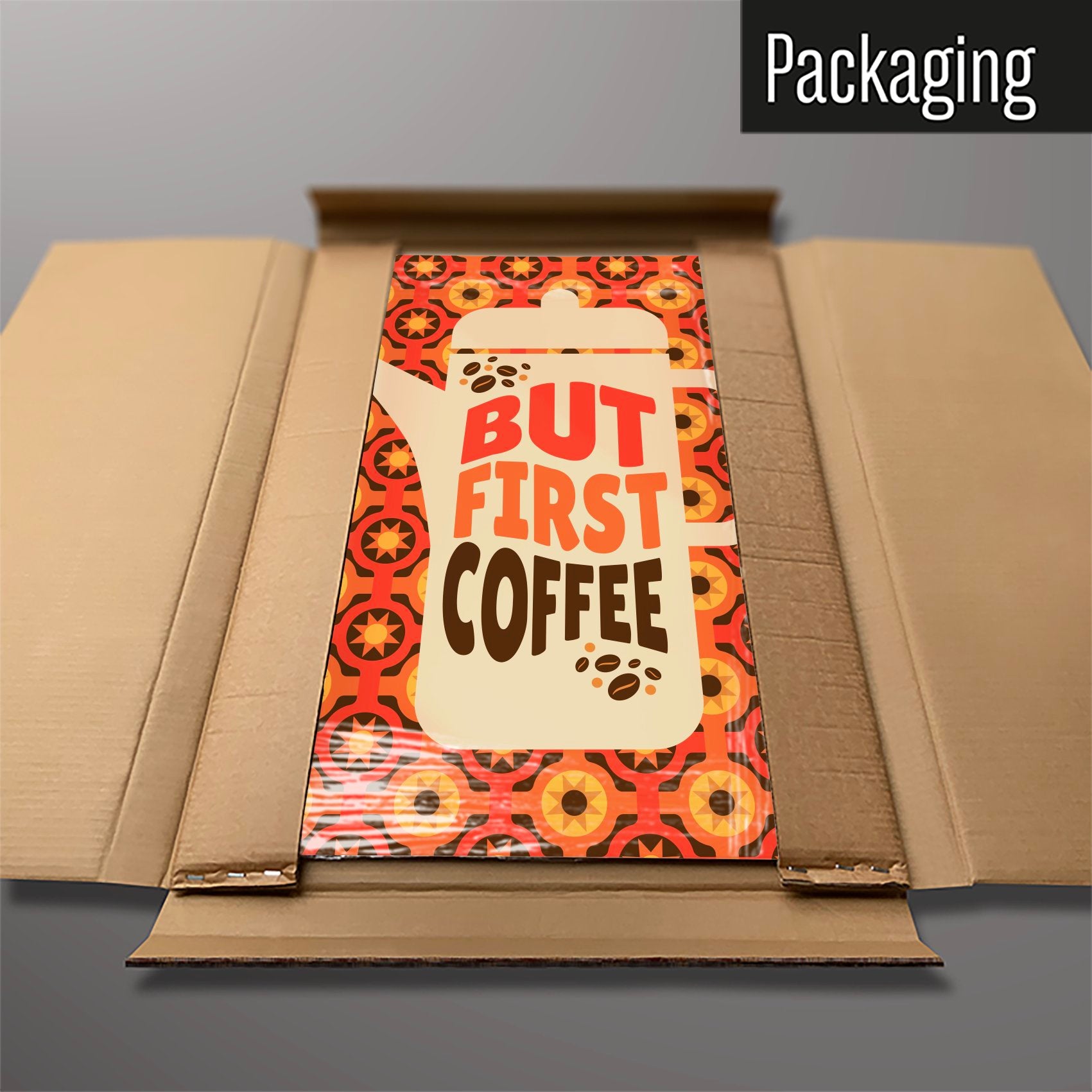 A large magnetic notice board showing a design of a  coffee pot with a quote that reads 'but first coffee' with a seventies style orange and brown pattern behind in cardboard packaging