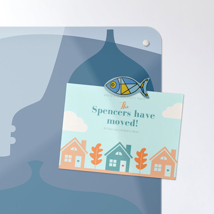 A postcard attached with a fish shaped fridge magnet on a blue bottles design magnetic board or metal wall art panel