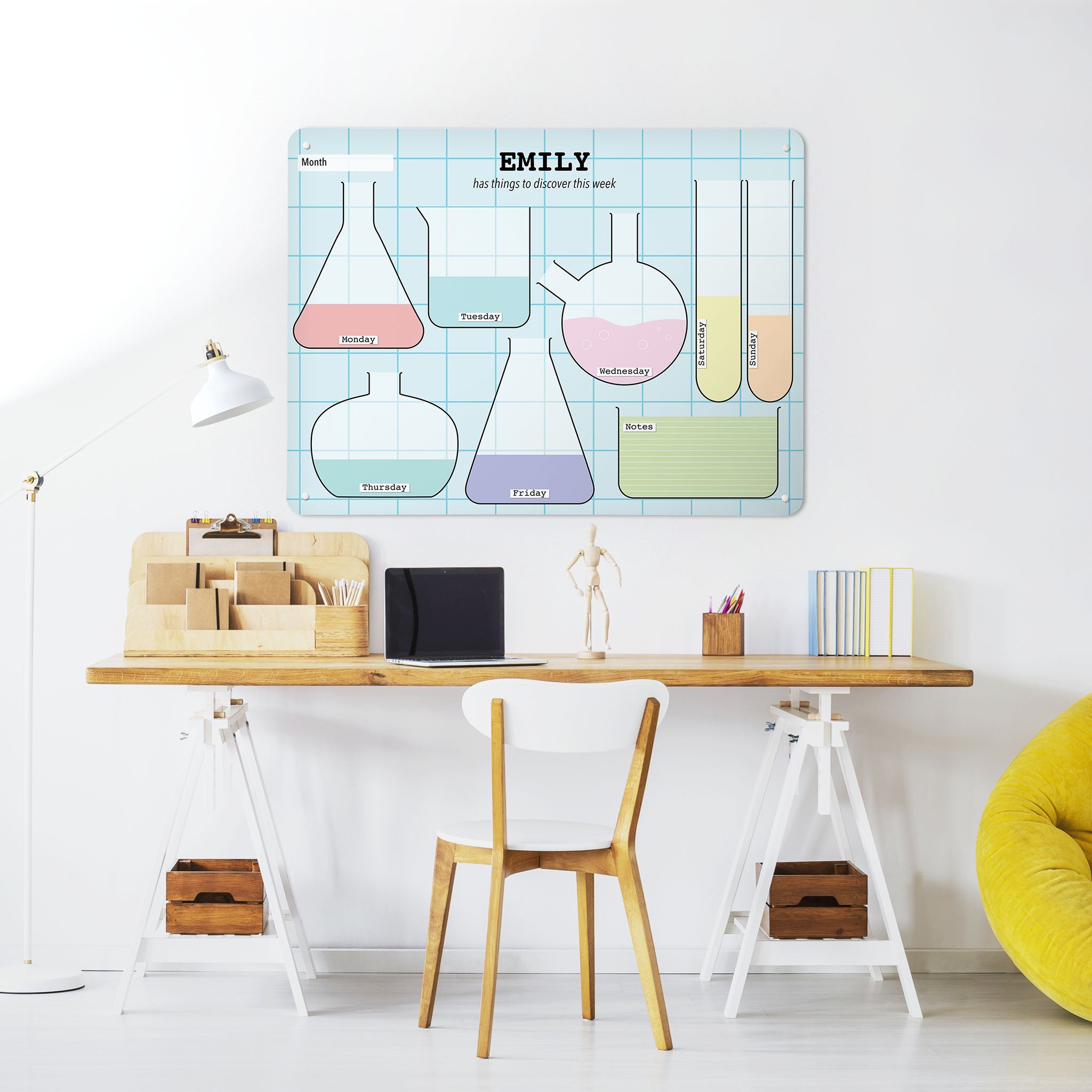 A desk in a workspace setting in a white interior with a magnetic metal wall art panel showing a science lab design weekly planner to personalise