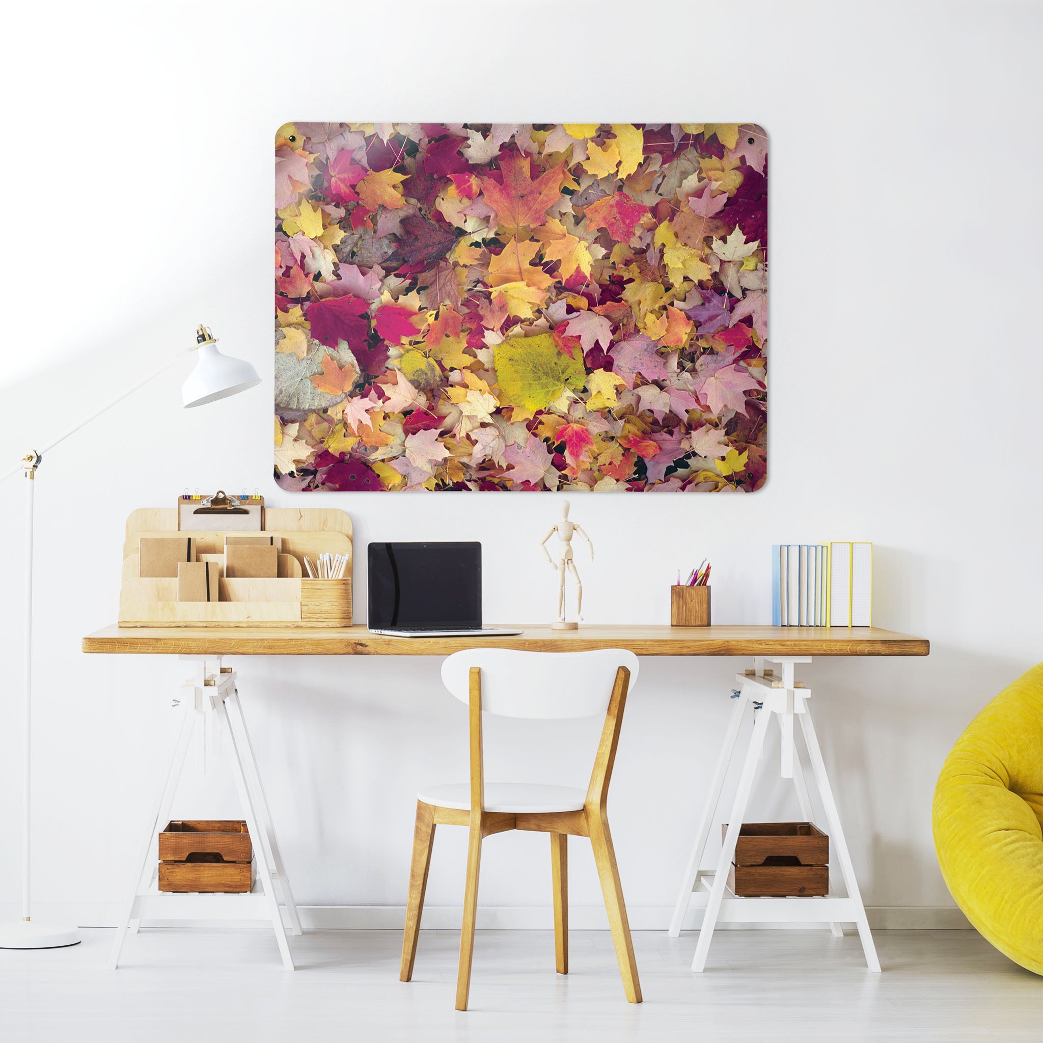 A desk in a workspace setting in a white interior with a magnetic metal wall art panel showing a photograph of autumn leaves