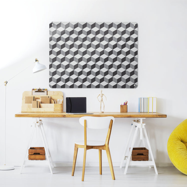 A desk in a workspace setting in a white interior with a magnetic metal wall art panel showing a shades of grey blocks design