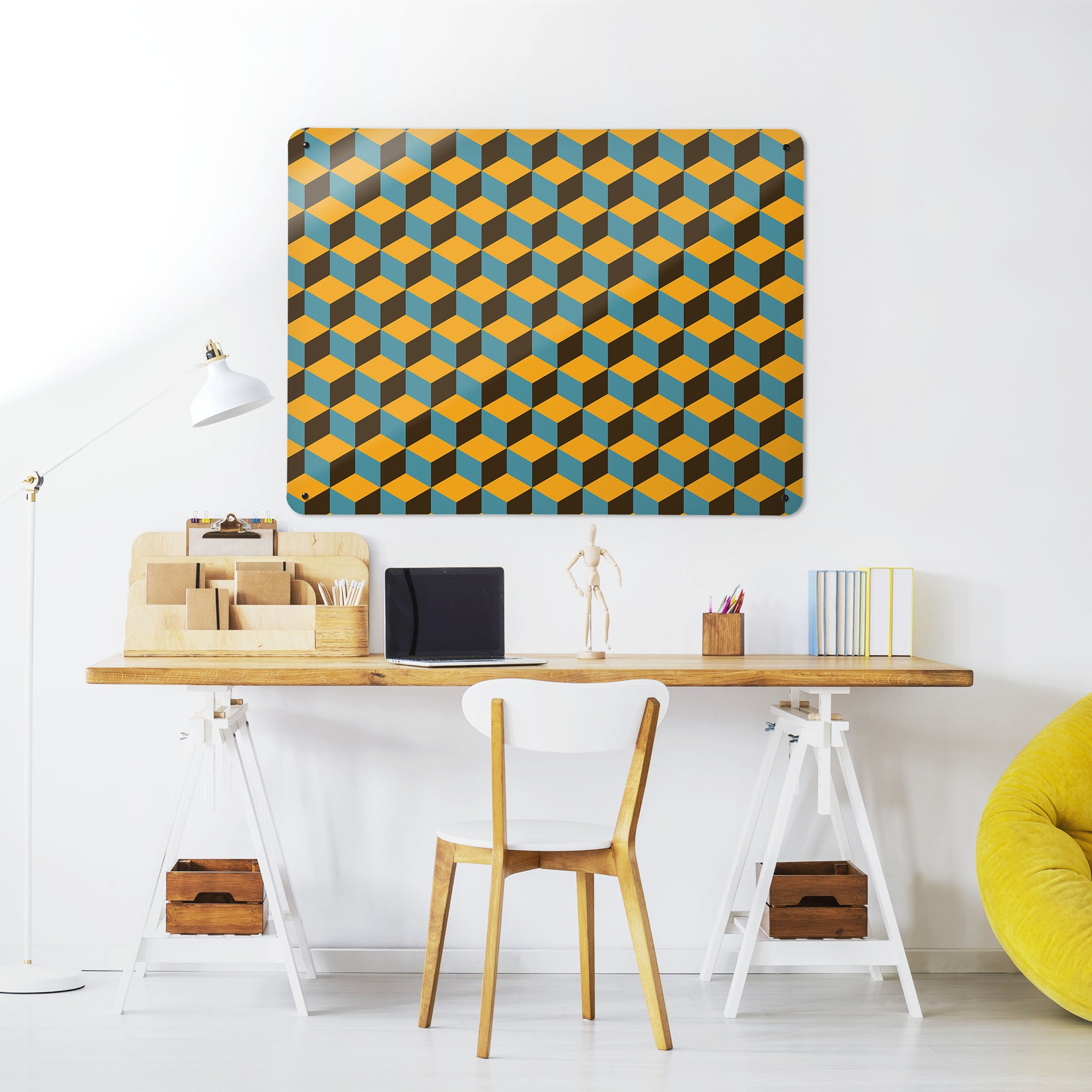 A desk in a workspace setting in a white interior with a magnetic metal wall art panel showing a mustard, blue and brown blocks design