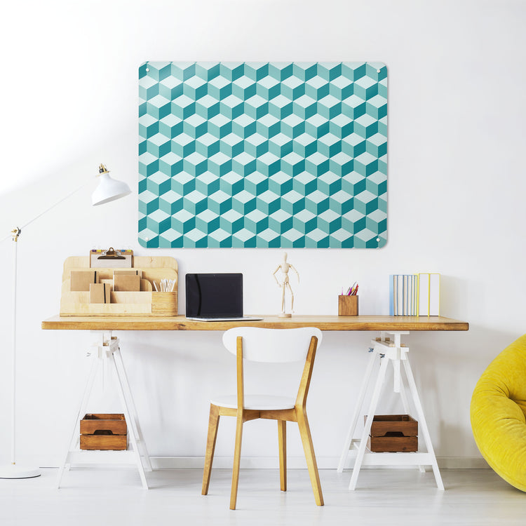 A desk in a workspace setting in a white interior with a magnetic metal wall art panel showing a shades of teal blocks design