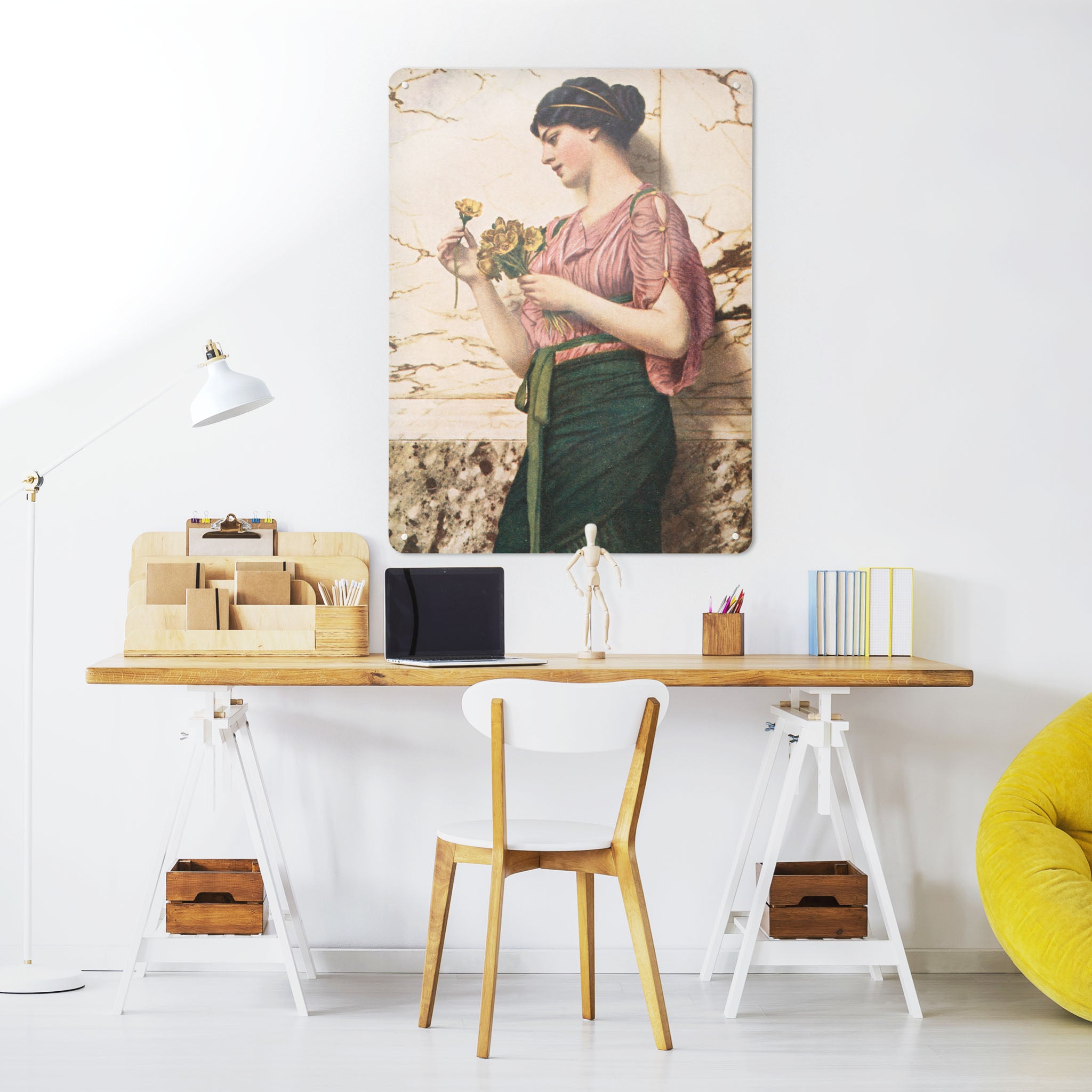 A desk in a workspace setting in a white interior with a magnetic metal wall art panel showing Crytilla a painting of a woman holding flowers