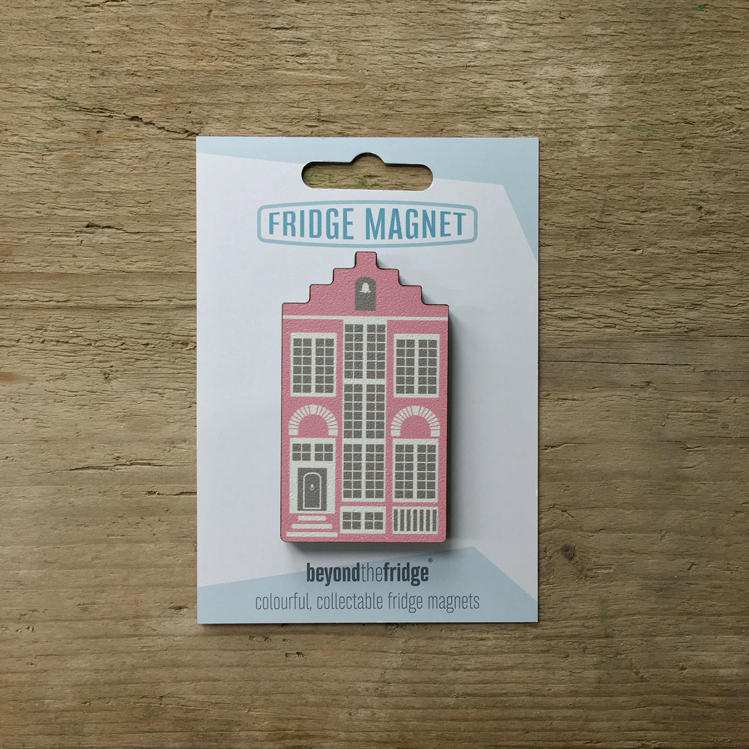 A pink Delft house shaped plywood fridge magnet by Beyond the Fridge in it’s pack on a wooden background