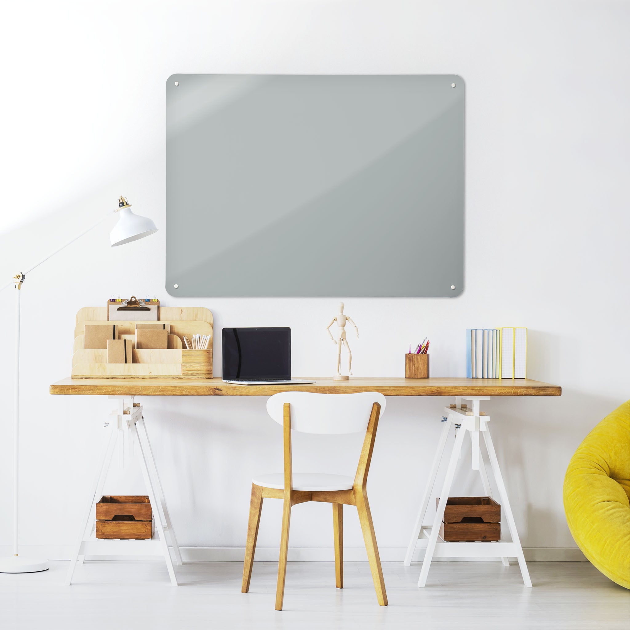 A desk in a workspace setting in a white interior with a plain grey coloured magnetic metal wall art panel
