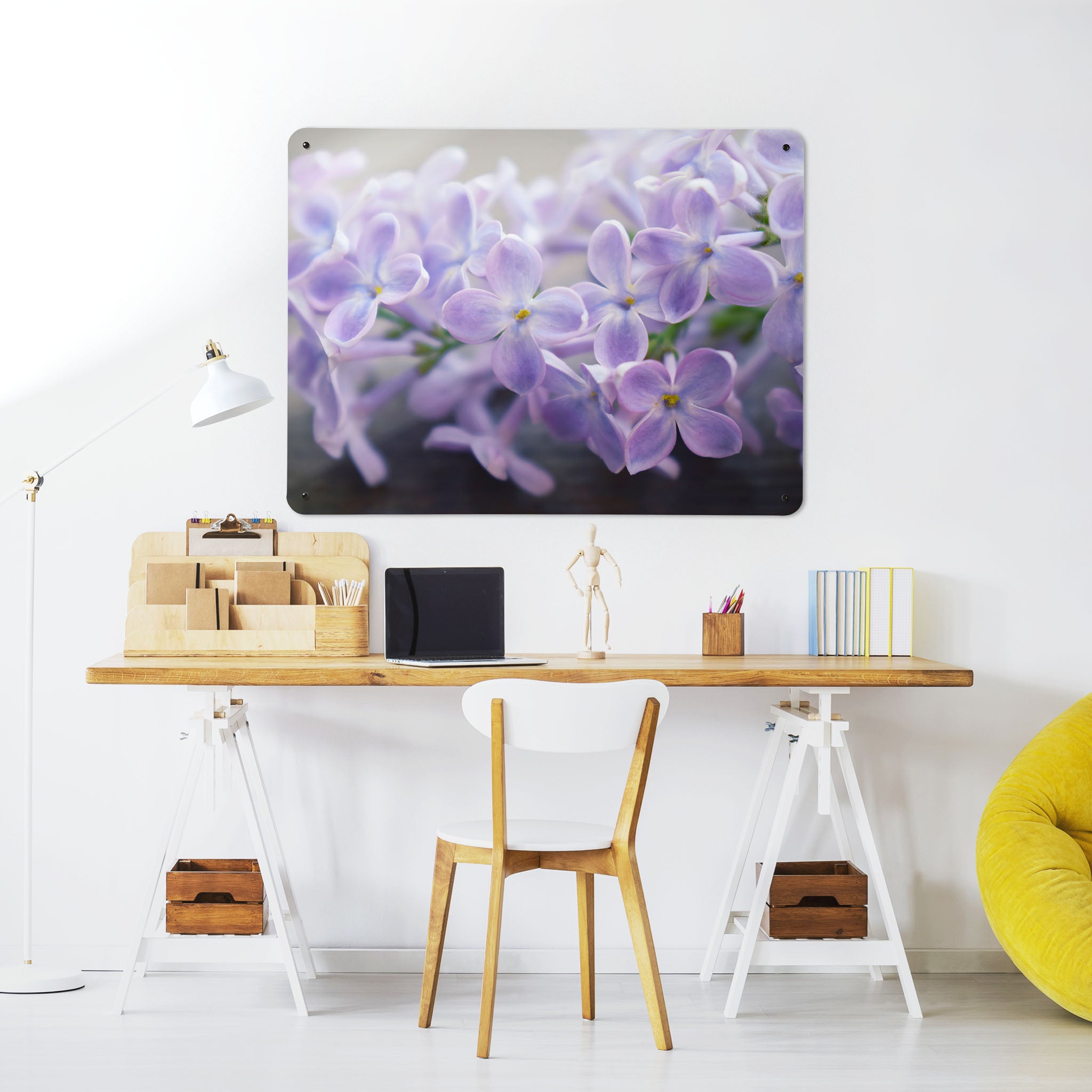 A desk in a workspace setting in a white interior with a magnetic metal wall art panel showing a photograph of lilac flowers