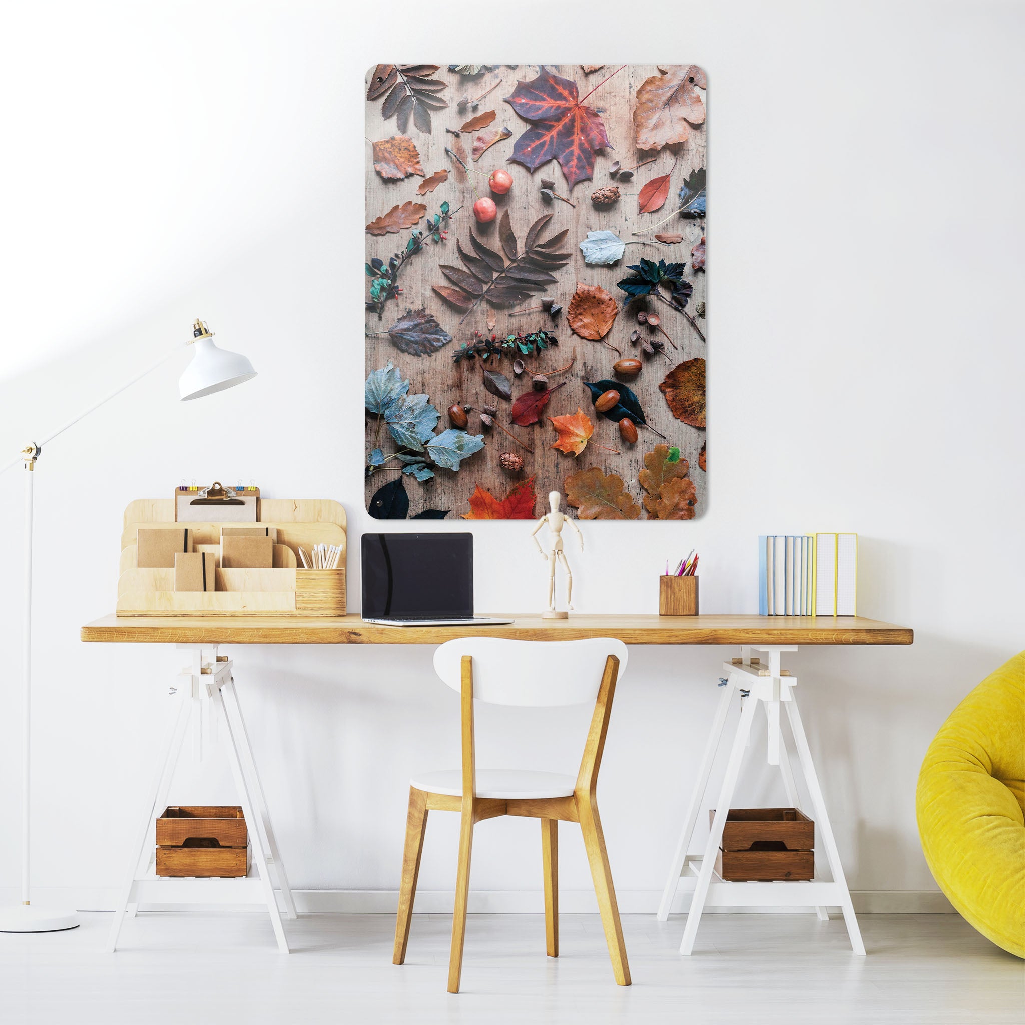 A desk in a workspace setting in a white interior with a magnetic metal wall art panel showing a flatly photograph of autumn leaves on a wood background