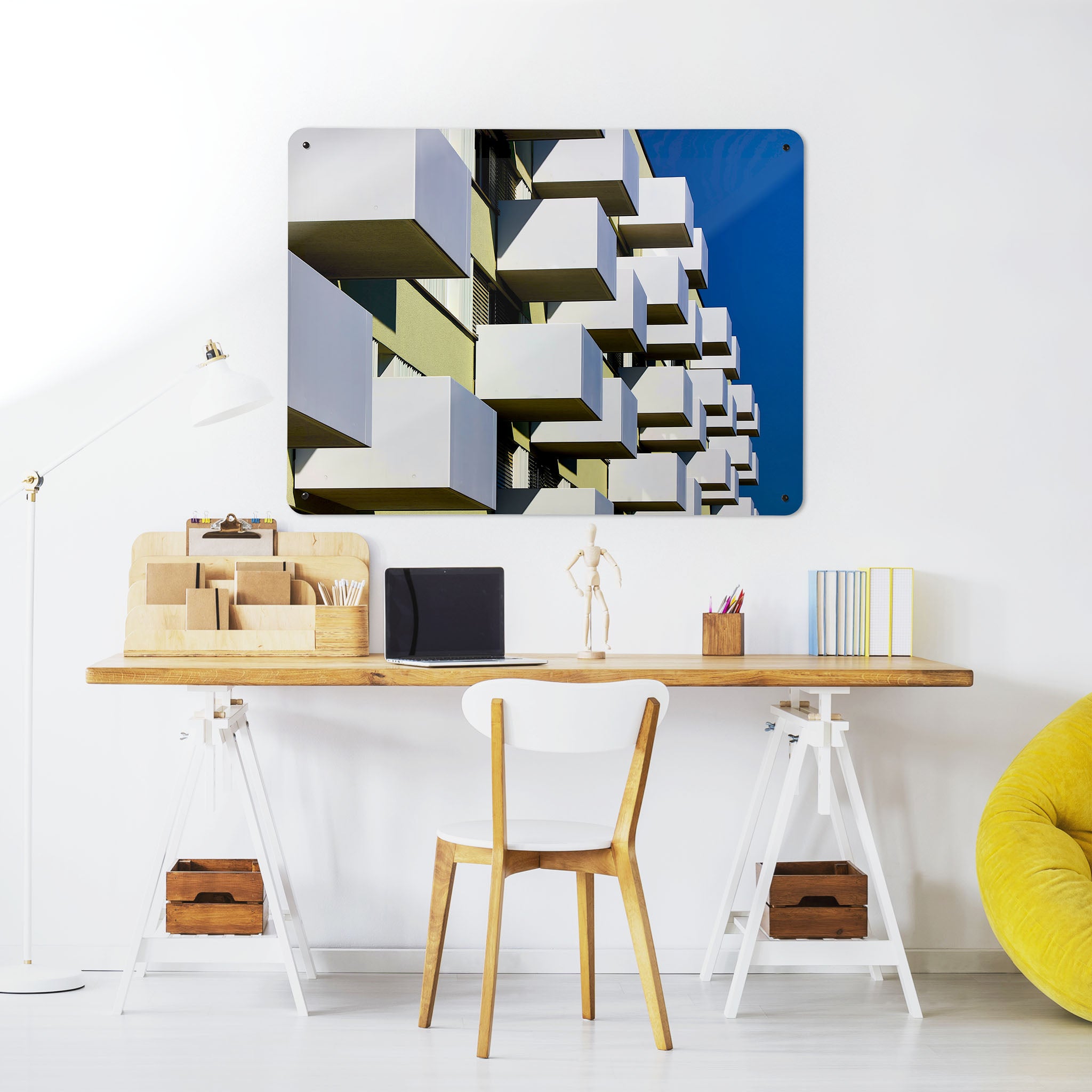 A desk in a workspace setting in a white interior with a magnetic metal wall art panel showing a photograph of brutalist balconies