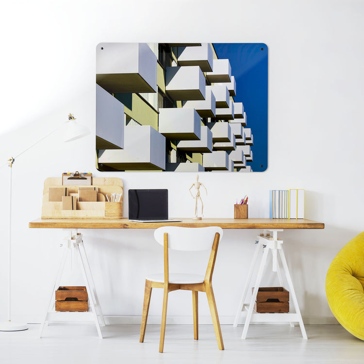 A desk in a workspace setting in a white interior with a magnetic metal wall art panel showing a photograph of brutalist balconies