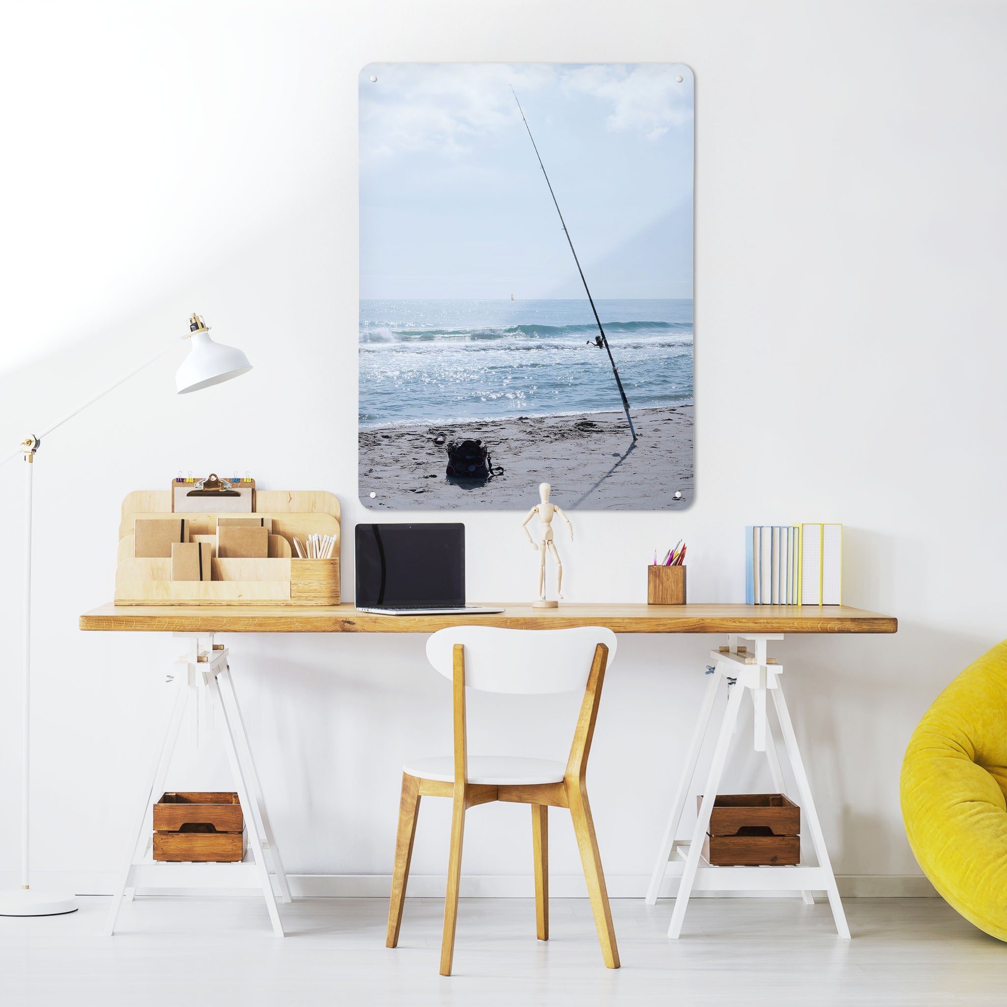 A desk in a workspace setting in a white interior with a magnetic metal wall art panel showing a photograph of fishing tackle on a sunny beach