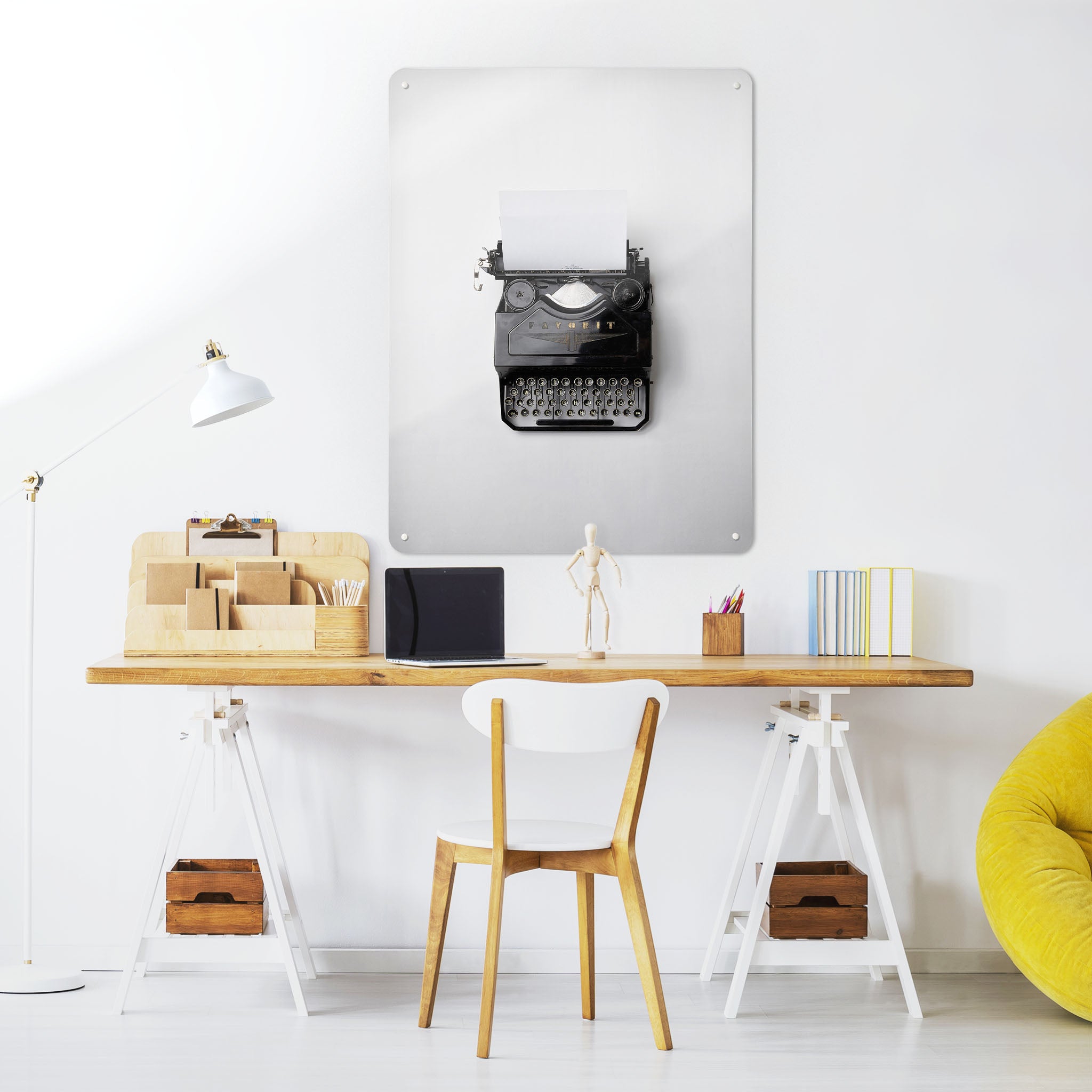 A desk in a workspace setting in a white interior with a magnetic metal wall art panel showing a photograph of a bird's eye view of a vintage typewriter on a white background