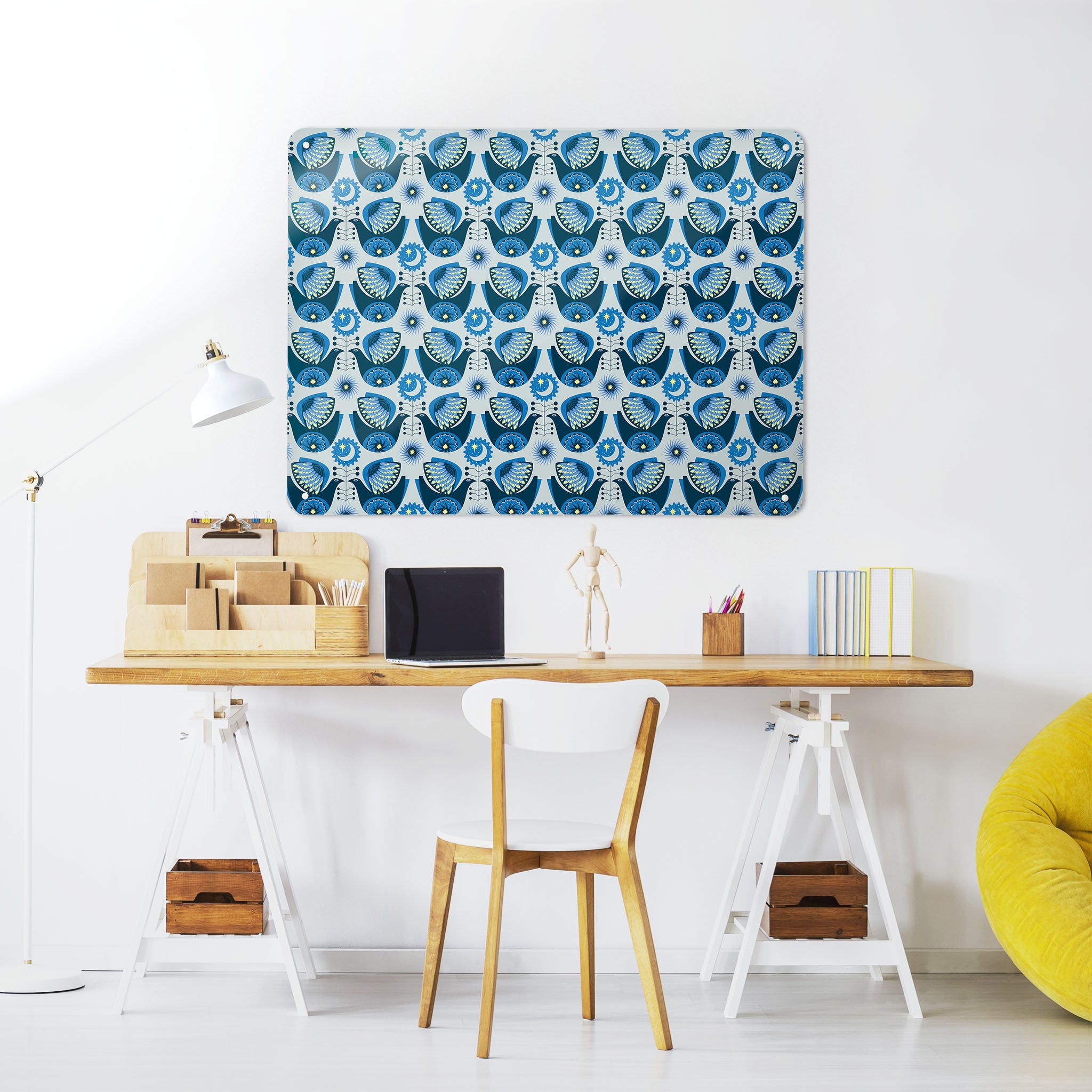 A desk in a workspace setting in a white interior with a magnetic metal wall art panel showing a retro night bird design