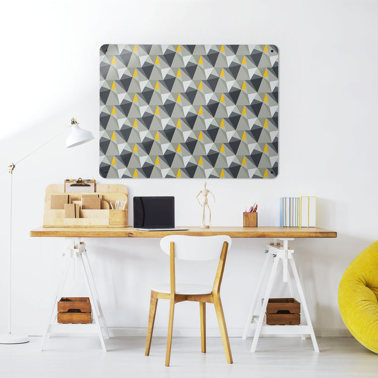A desk in a workspace setting in a white interior with a magnetic metal wall art panel showing a shards design in concrete and yellow colour way