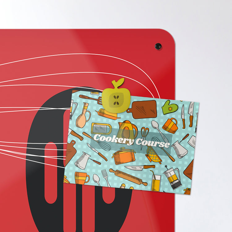 A postcard attached with an apple shaped fridge magnet on a red utensils design magnetic board or metal wall art panel