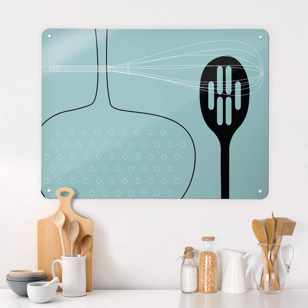 A kitchen interior with a magnetic metal wall art panel showing a blue utensils design