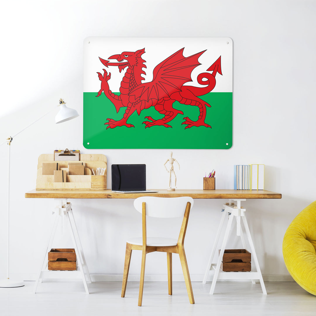 A desk in a workspace setting in a white interior with a magnetic metal wall art panel with a Welsh Flag design