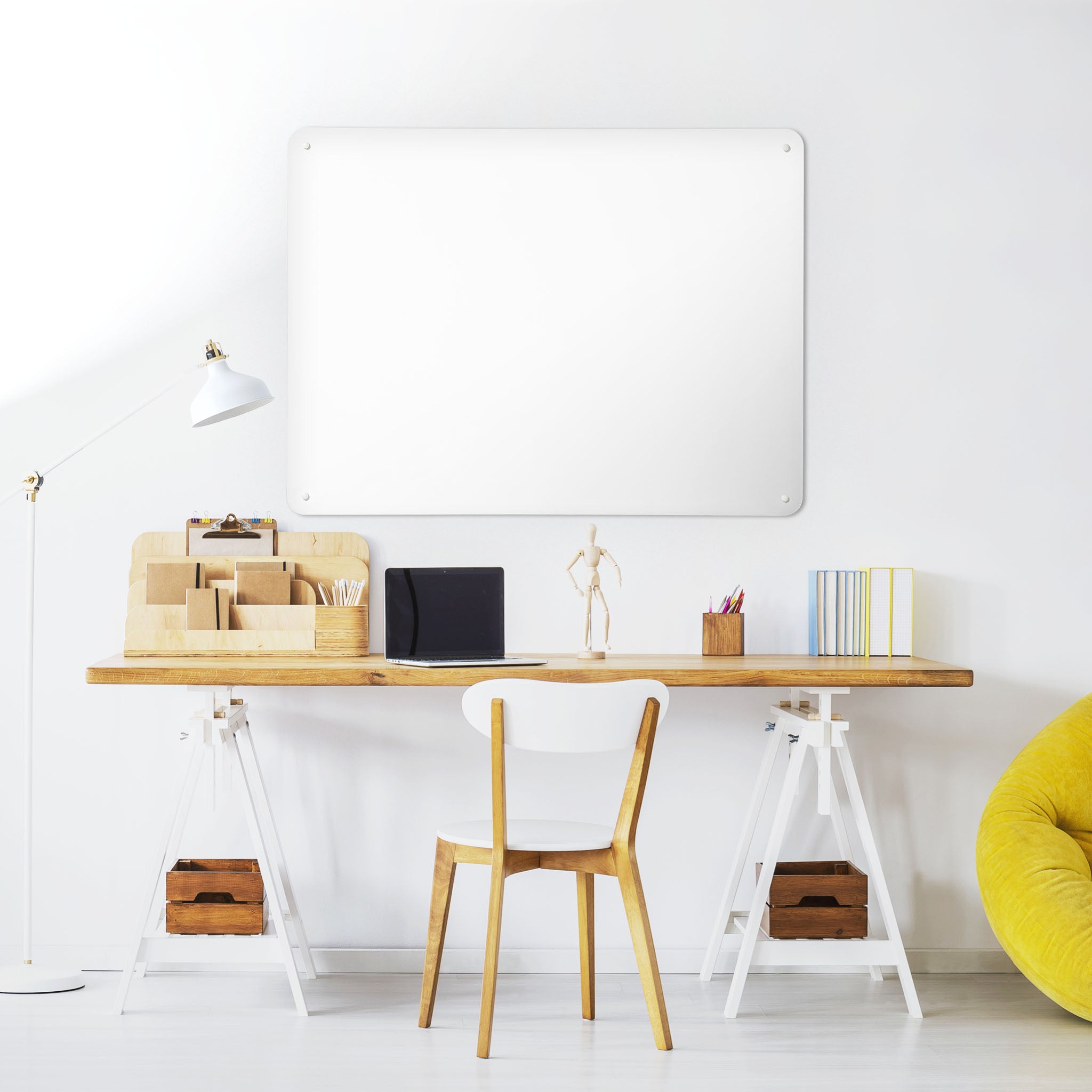 A desk in a workspace setting in a white interior with a plain white magnetic metal wall art panel