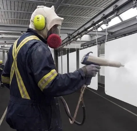 A coater in respirator and ear defenders spraying a panel on the coating line