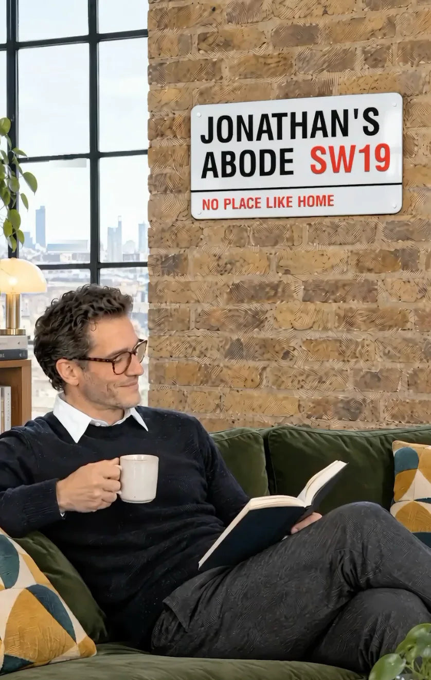 A man reading on a green sofa under a personalised street sign reading Jonathan's Abode SW19