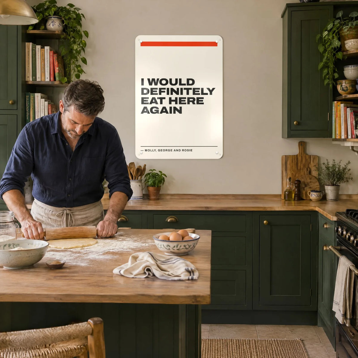 A man rolling pastry in a kitchen with green cabinets under a quote board reading I would definitely eat here again