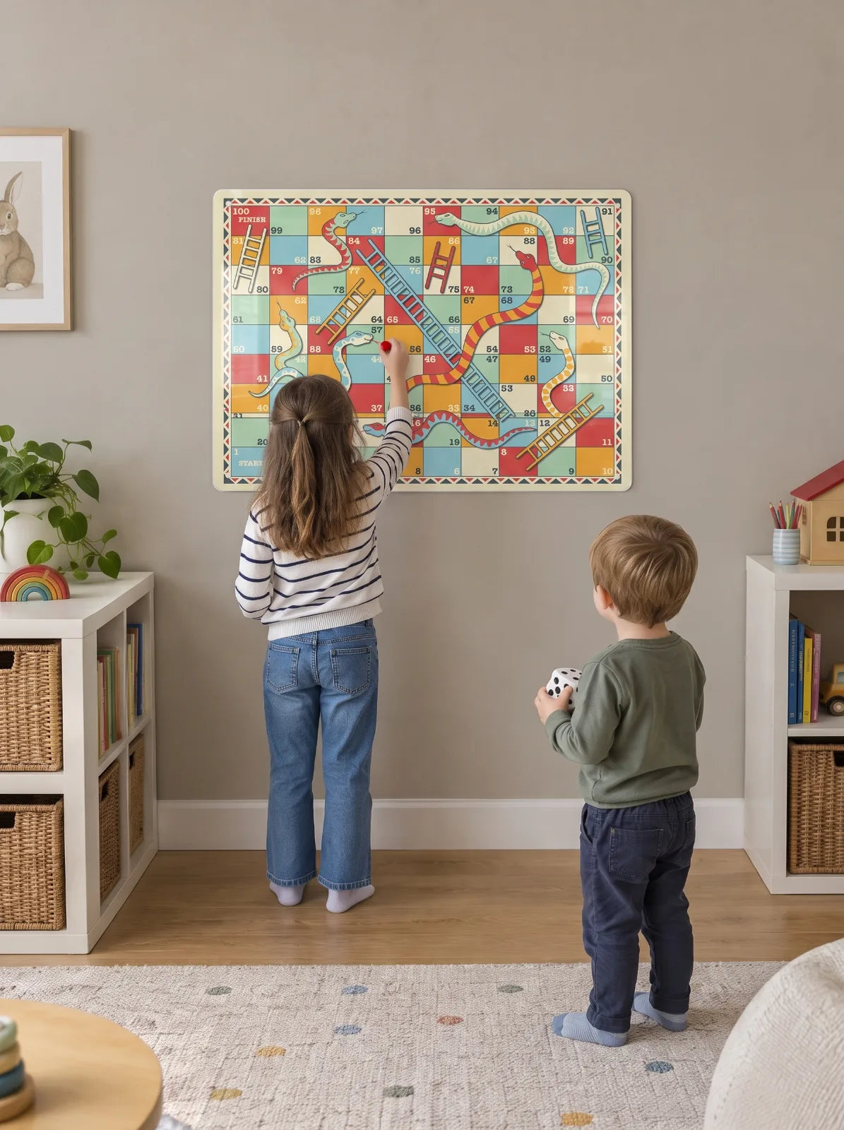Two children playing on a Snakes and Ladders board on a playroom wall