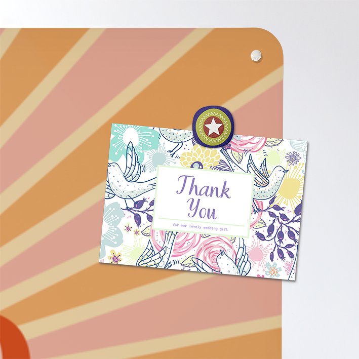 Close up of the corner of large steel magnetic board with a print of a typographic quote design that reads Hello Sunshine with a sunburst in pink and orange colours with a postcard attached with a colourful magnet