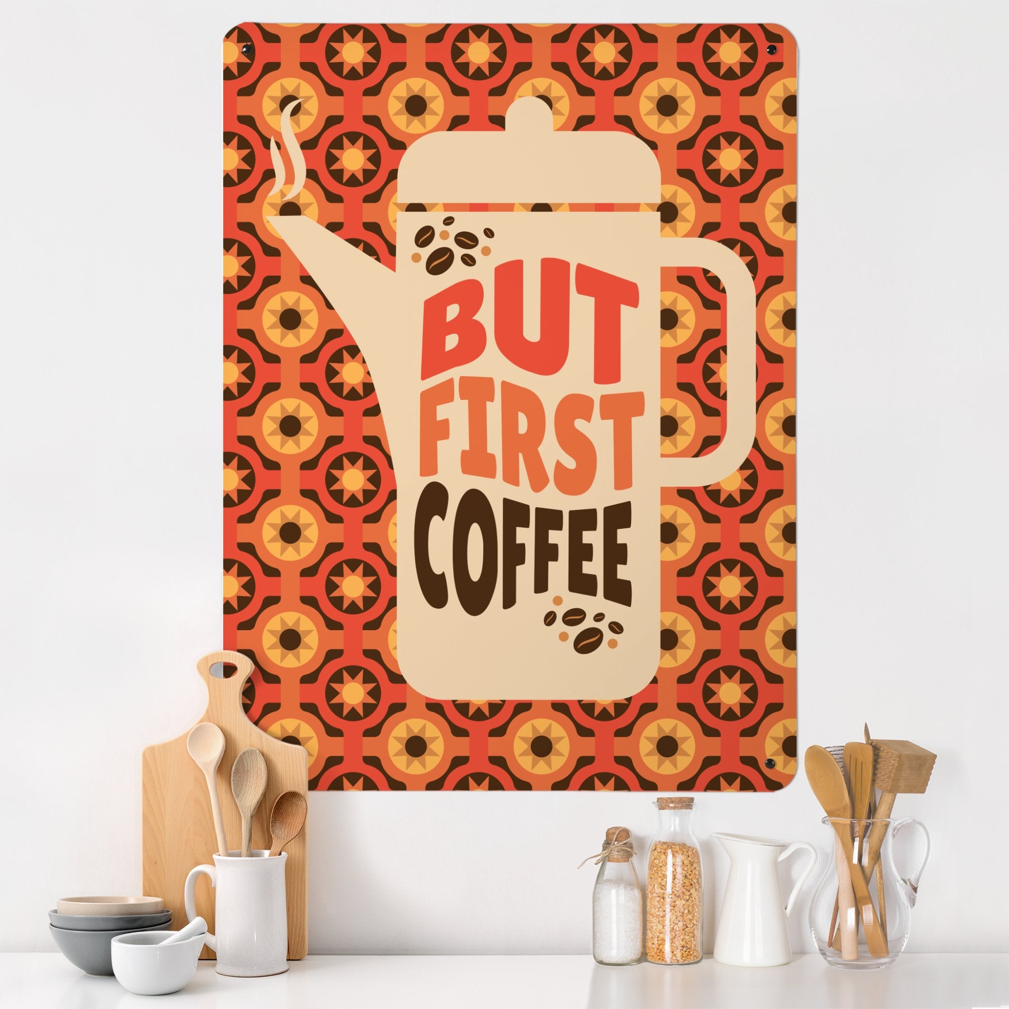 A large magnetic notice board showing a design of a  coffee pot with a quote that reads 'but first coffee' with a seventies style orange and brown pattern behind in a kitchen setting with wooden spoons and other kitchen utensils