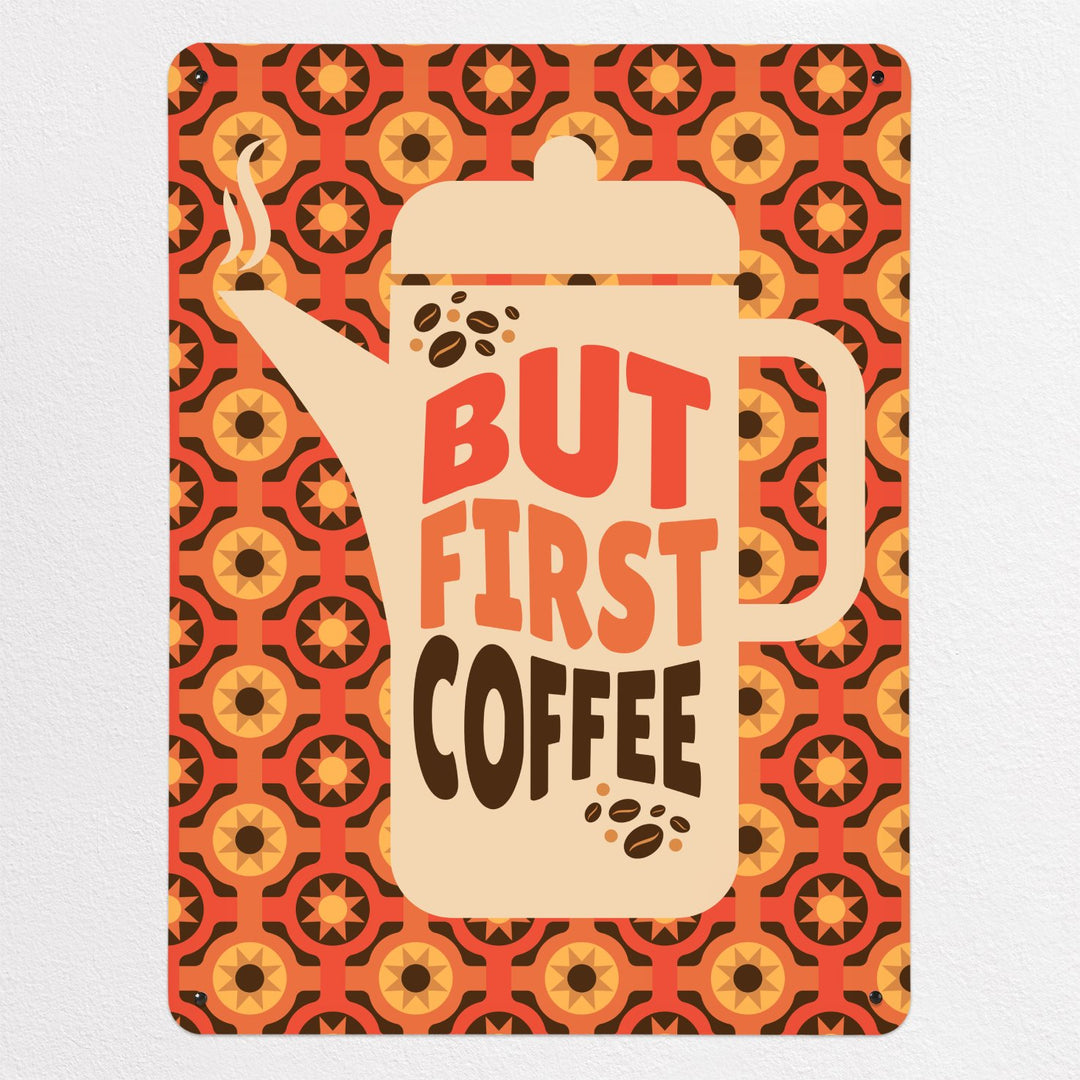 A large magnetic notice board showing a design of a  coffee pot with a quote that reads 'but first coffee' with a seventies style orange and brown pattern behind