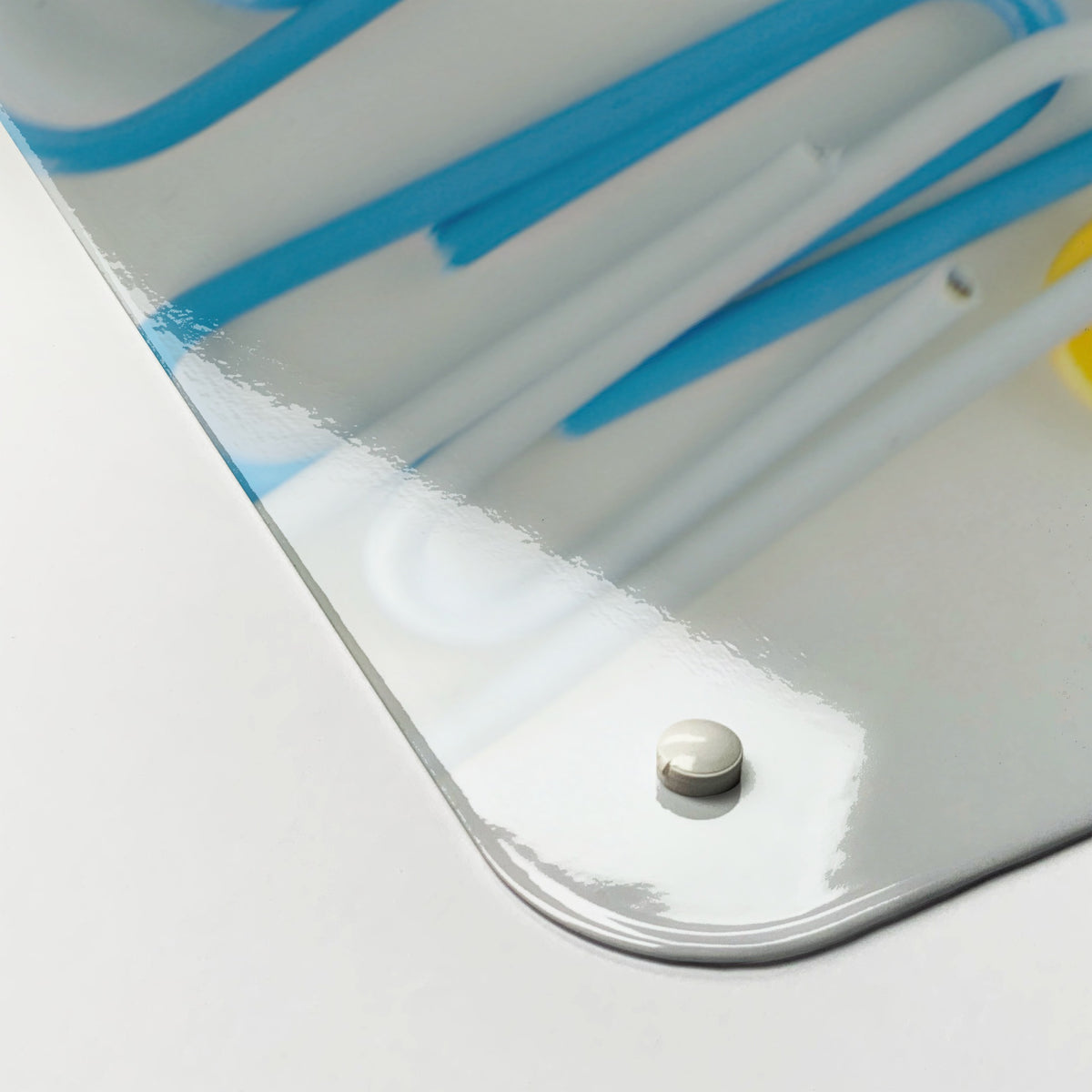 Close-up of the corner of the Paper Clips magnetic notice board in Paper Clips, showing the gloss finish and a screw cap