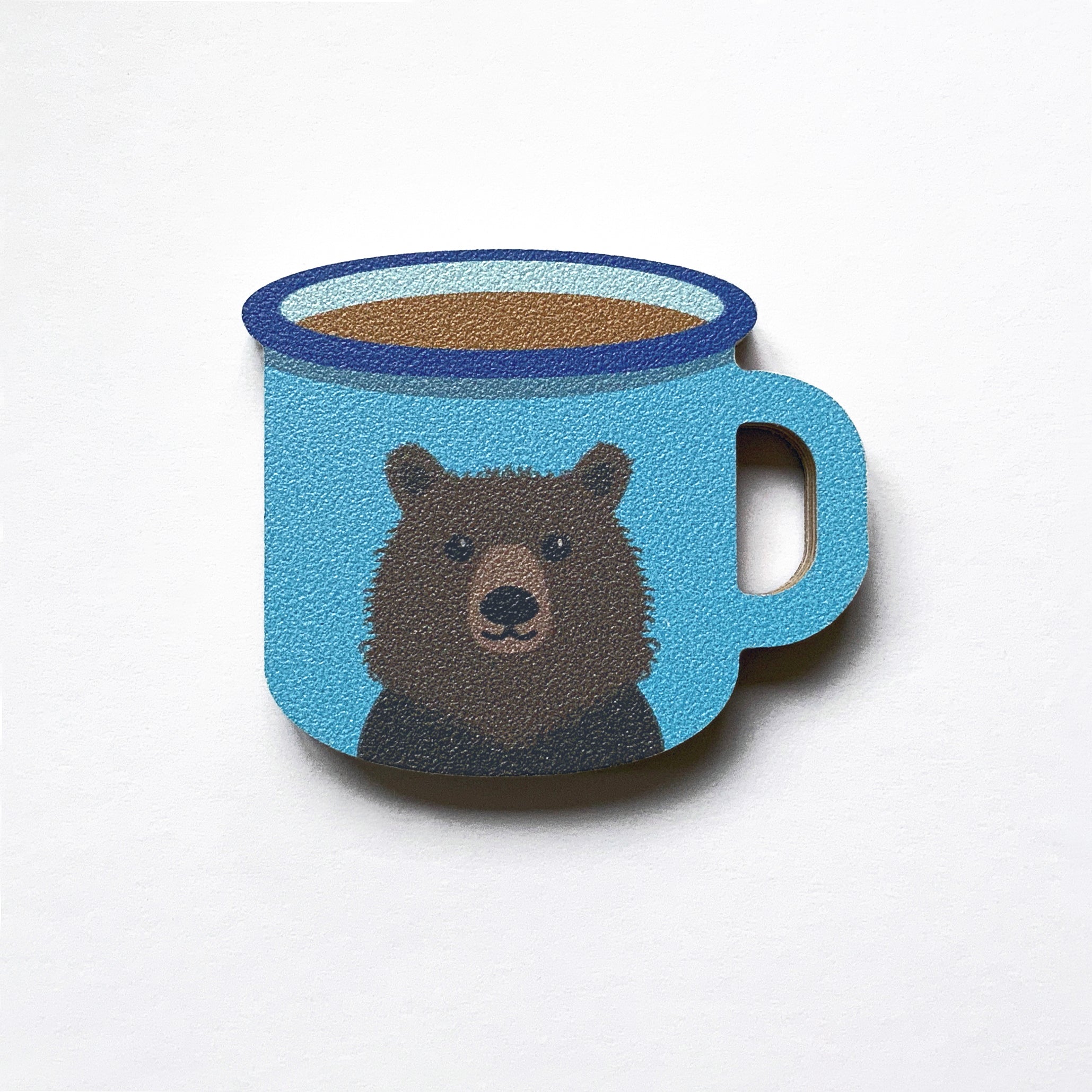An enamel mug shaped plywood fridge magnet by Beyond the Fridge with an illustration of a brown bear on a blue background