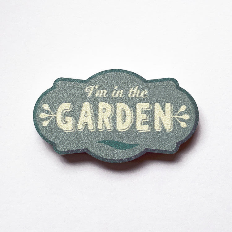 A vintage label shaped plywood fridge magnet by Beyond the Fridge with type that says I'm in the garden