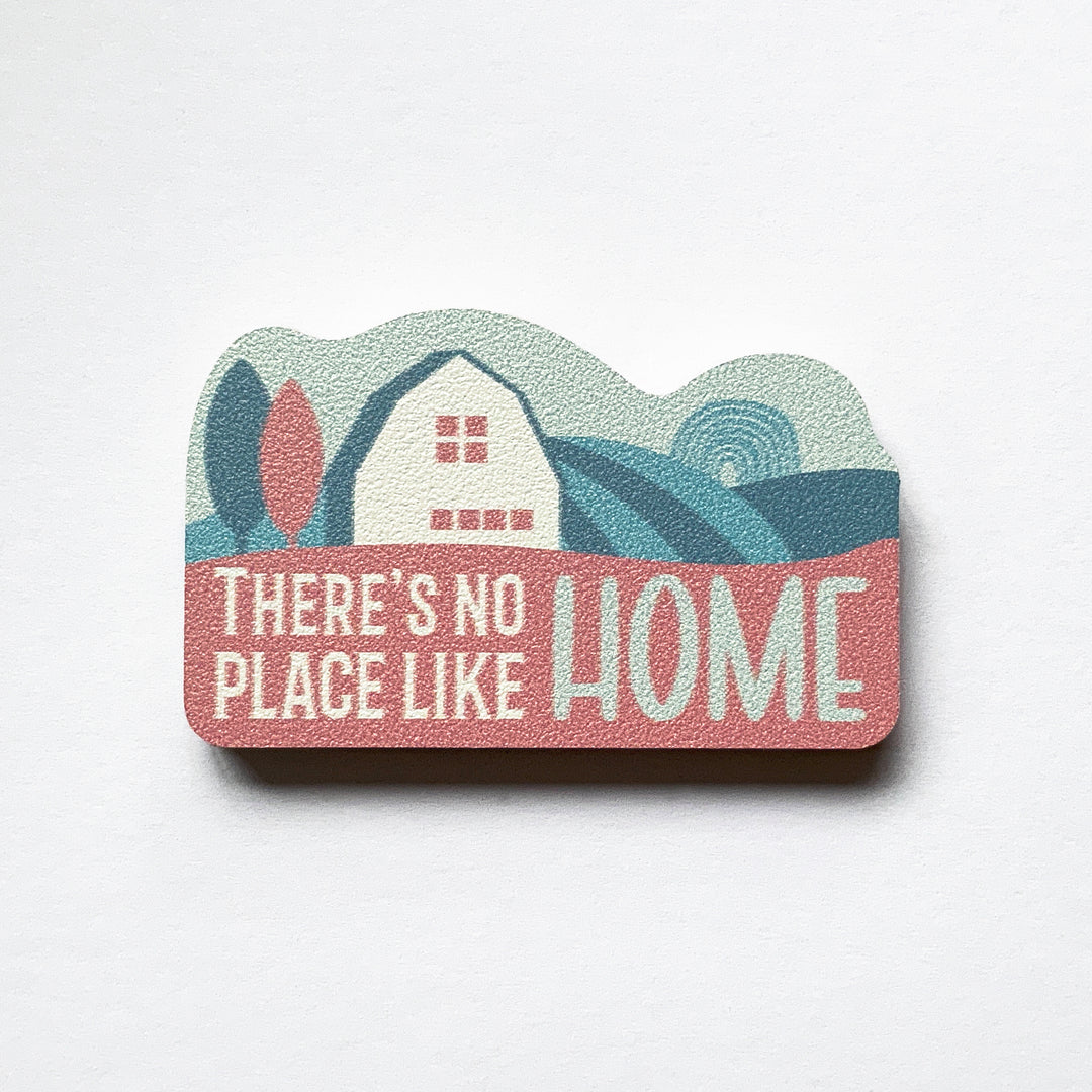 A vintage label shaped plywood fridge magnet by Beyond the Fridge with type that says there's no place like home