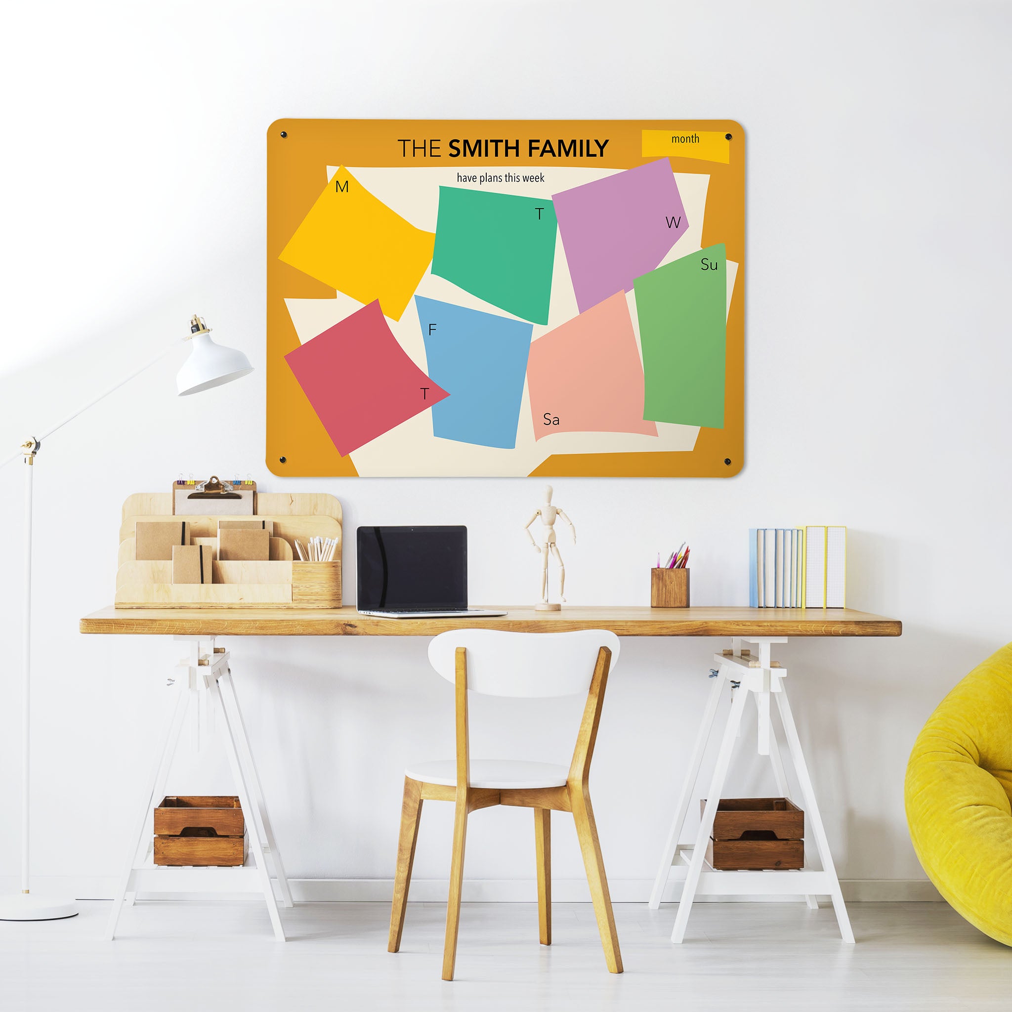 A desk in a workspace setting in a white interior with a magnetic metal wall art panel showing a Henri Matisse design weekly planner to personalise