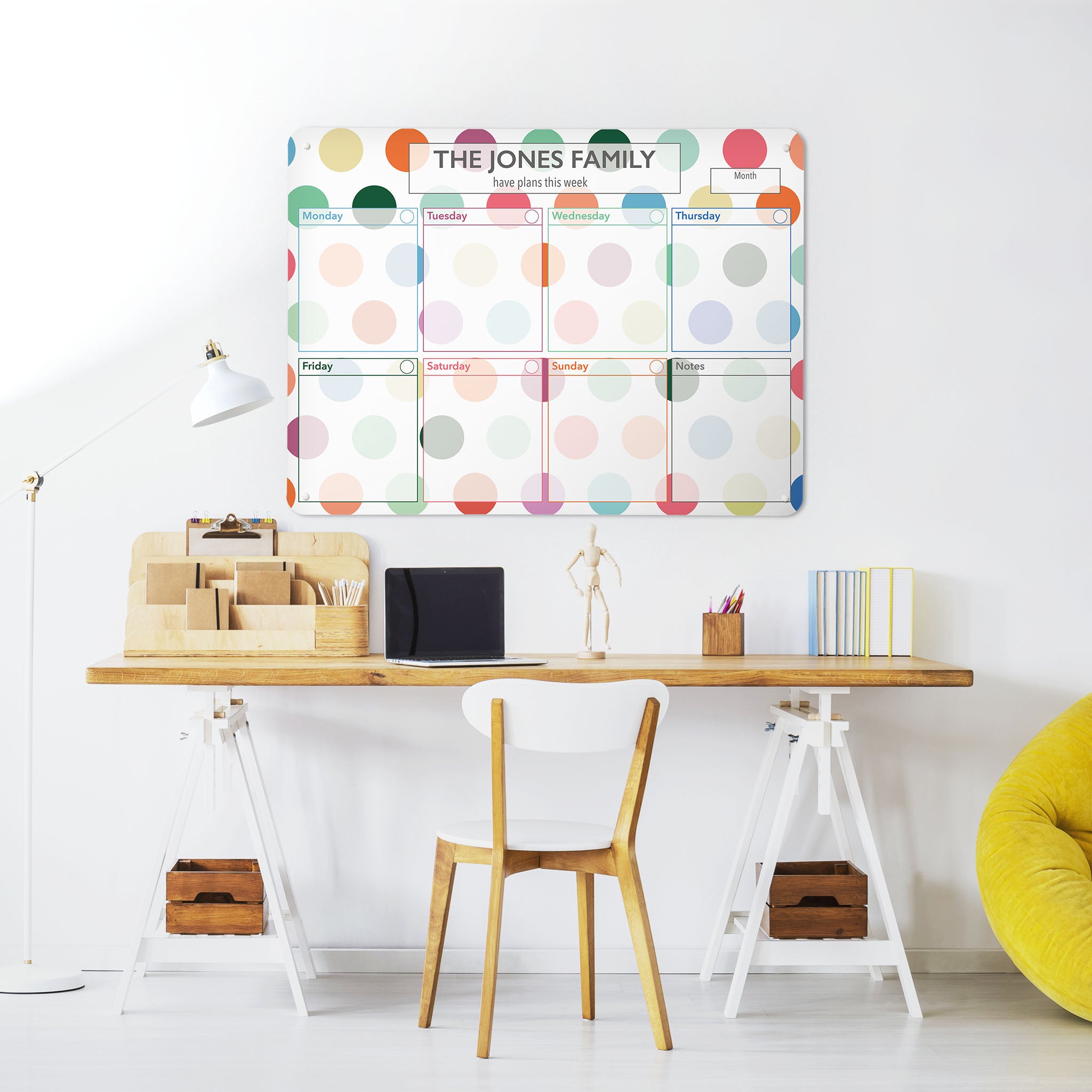 A desk in a workspace setting in a white interior with a magnetic metal wall art panel showing a spots design weekly planner to personalise