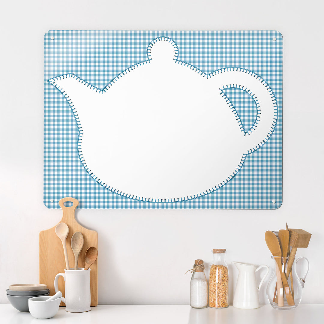 A  kitchen interior with a magnetic metal wall art panel showing an appliqué teapot design in white on a blue gingham background