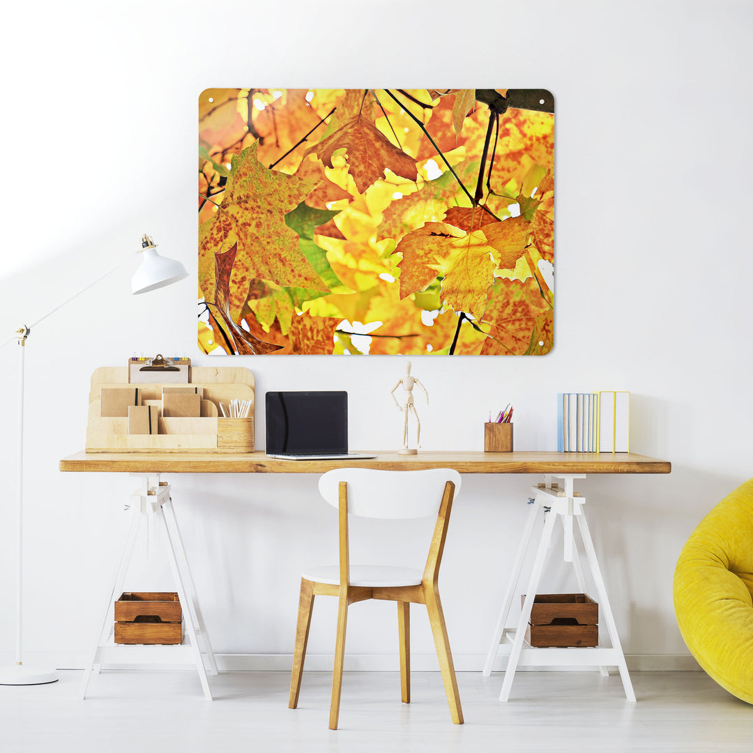 A desk in a workspace setting in a white interior with a magnetic metal wall art panel showing an autumn tree with yellow leaves