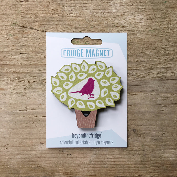 A bird in a tree shaped plywood fridge magnet by Beyond the Fridge in it’s pack on a wooden background