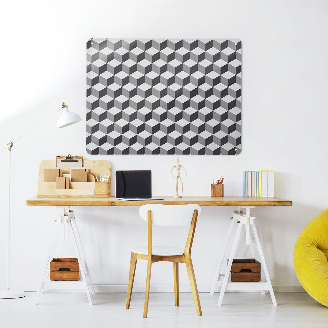 A desk in a workspace setting in a white interior with a magnetic metal wall art panel showing a shades of grey blocks design 