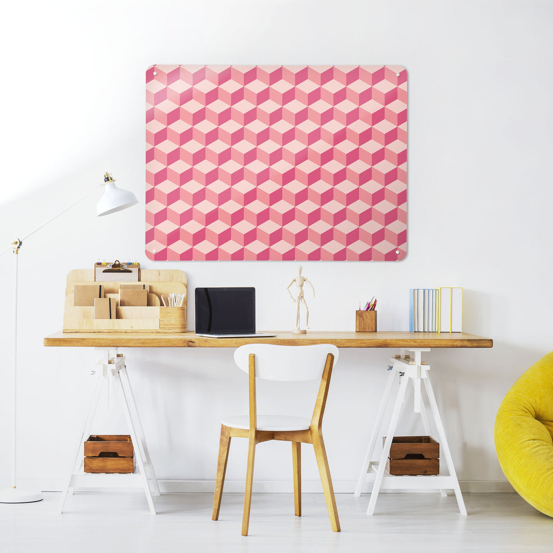 A desk in a workspace setting in a white interior with a magnetic metal wall art panel showing a shades of pink blocks design 