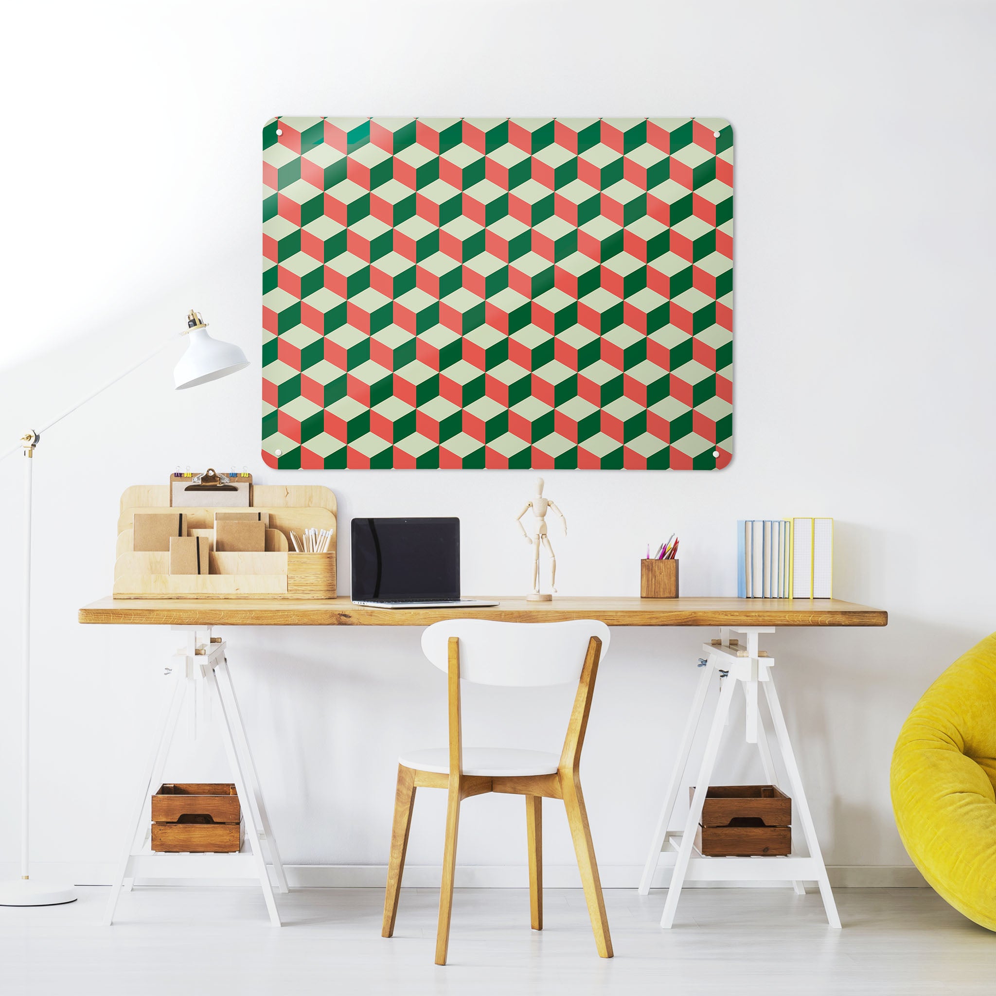A desk in a workspace setting in a white interior with a magnetic metal wall art panel showing a red, green and cream blocks design 