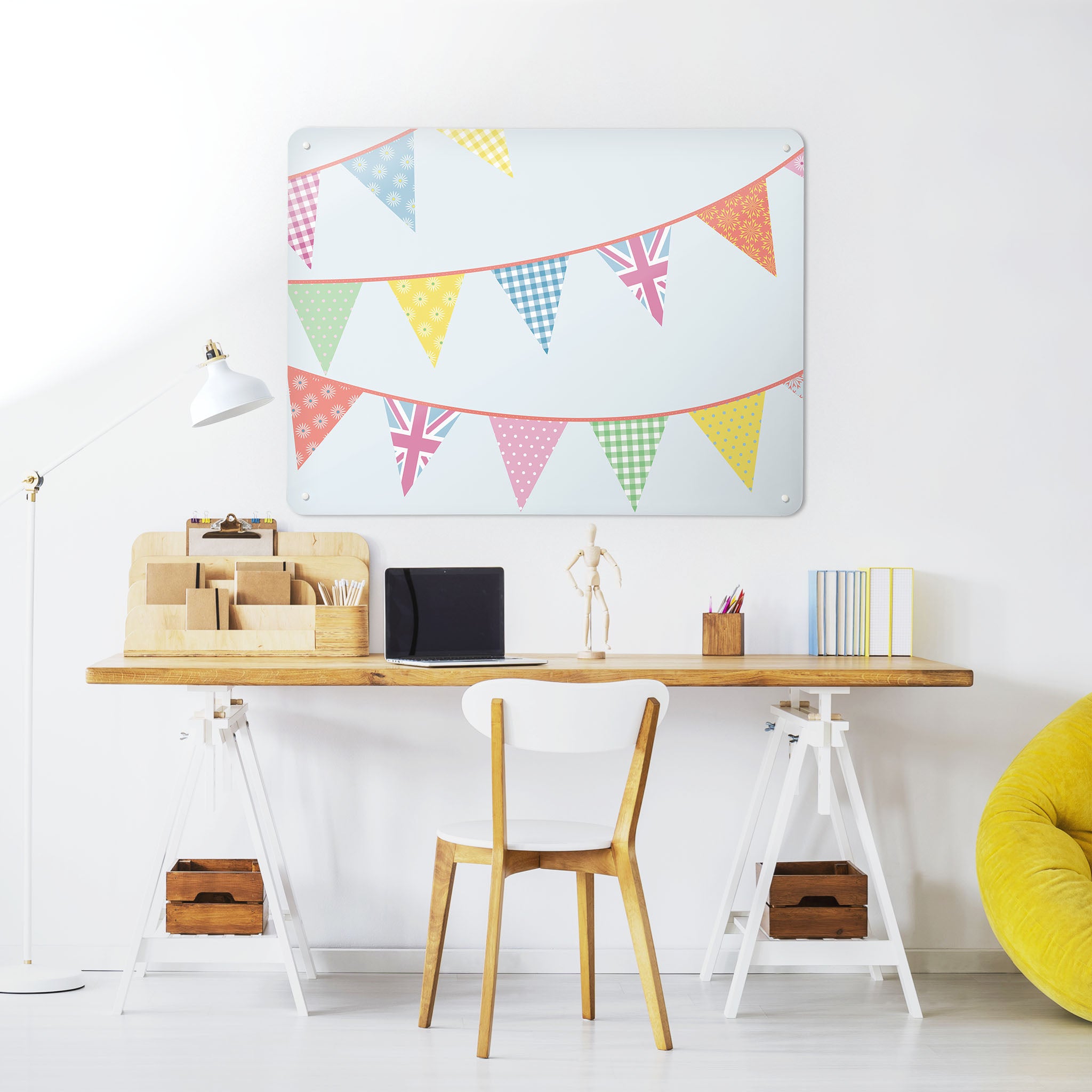 A desk in a workspace setting in a white interior with a magnetic metal wall art panel showing a bunting design in pastel colours