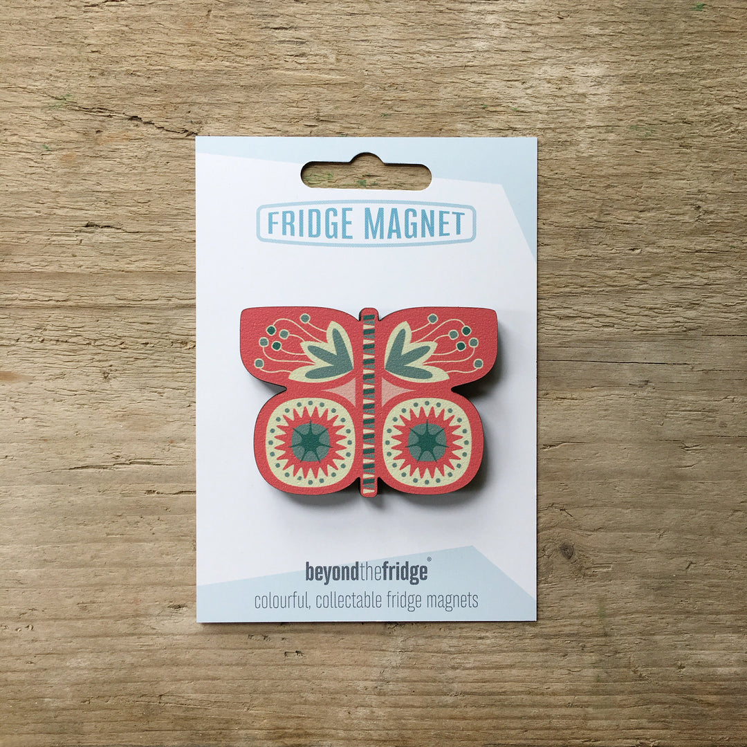 A pink butterfly shaped plywood fridge magnet by Beyond the Fridge in it’s pack on a wooden background