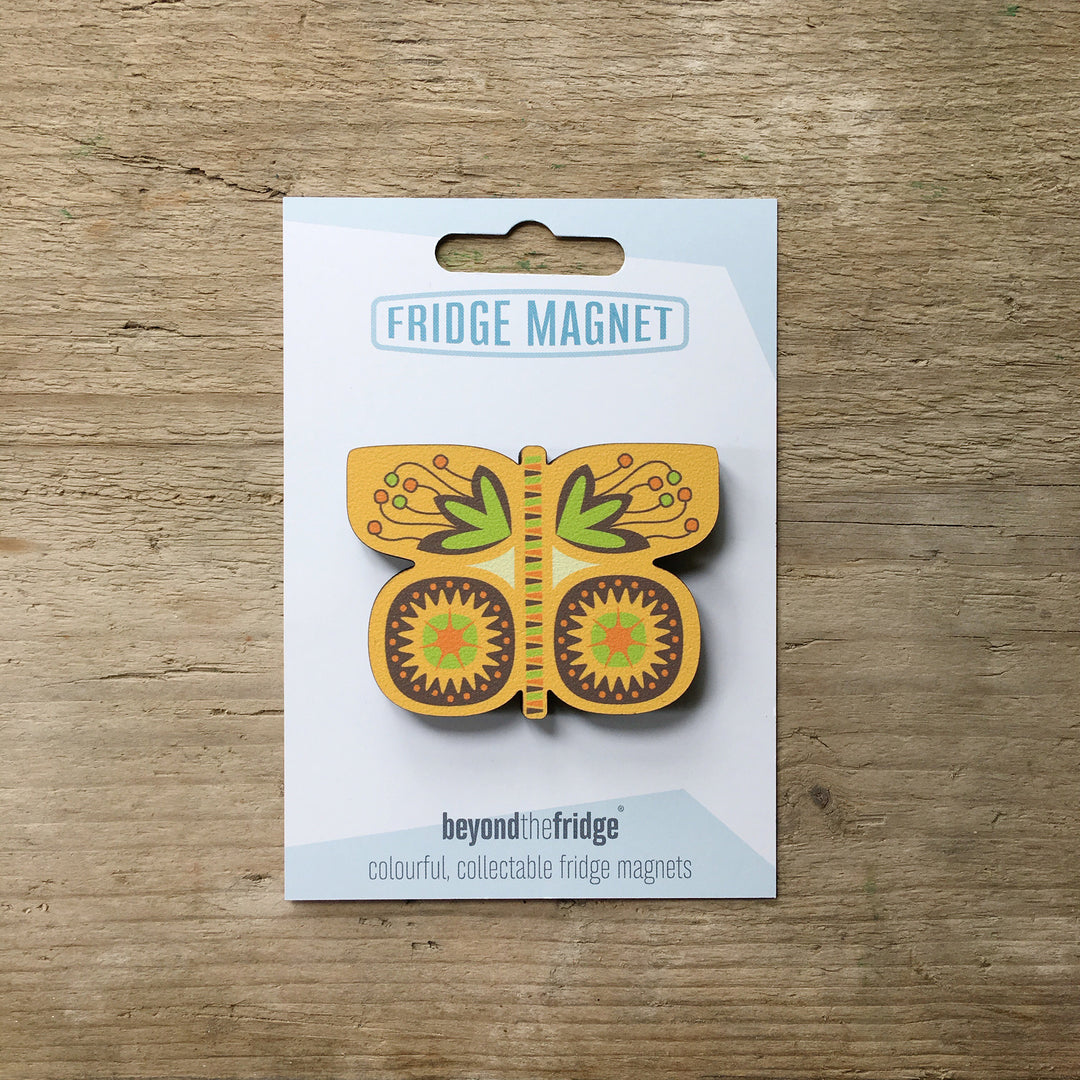A yellow butterfly shaped plywood fridge magnet by Beyond the Fridge in it’s pack on a wooden background