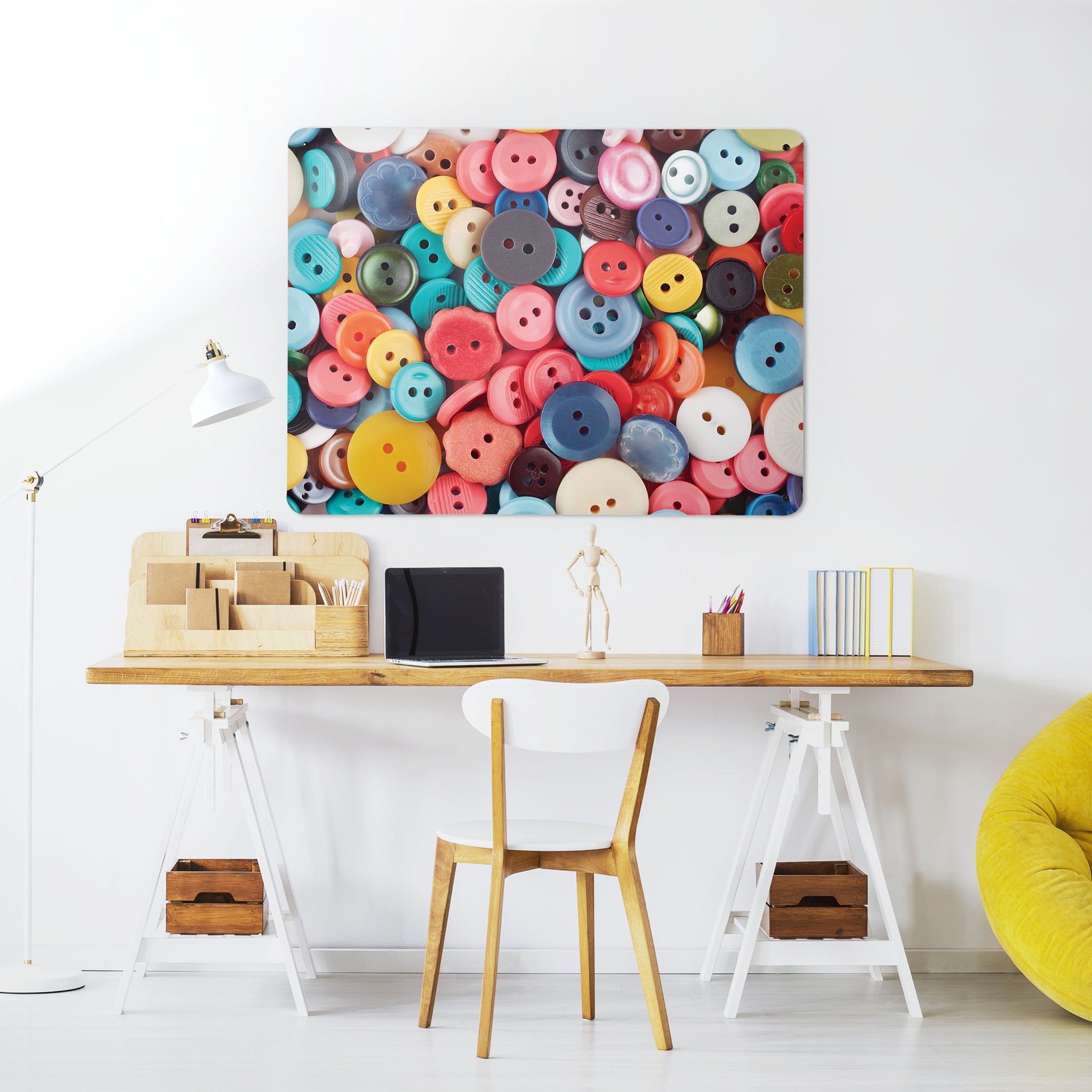 A desk in a workspace setting in a white interior with a magnetic metal wall art panel showing a colourful array of buttons