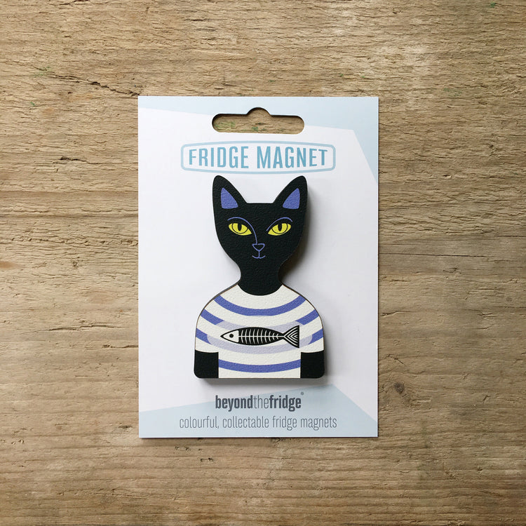 A black cat in a t-shirt shaped plywood fridge magnet by Beyond the Fridge in it’s pack on a wooden background