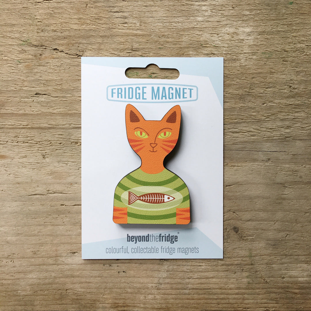 A ginger cat in a t-shirt shaped plywood fridge magnet by Beyond the Fridge in it’s pack on a wooden background
