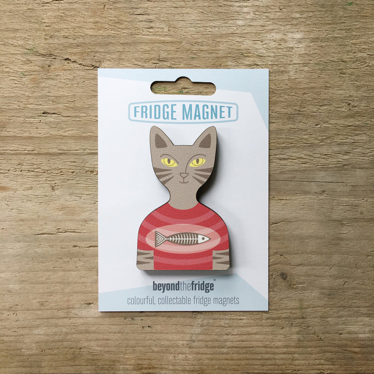A tabby cat in a t-shirt shaped plywood fridge magnet by Beyond the Fridge in it’s pack on a wooden background