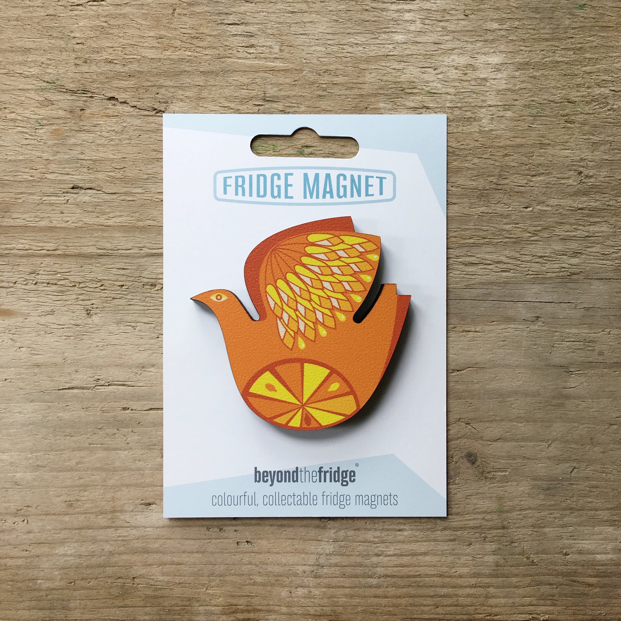 A retro citrus bird orange and lemon design plywood fridge magnet by Beyond the Fridge in it’s pack on a wooden background